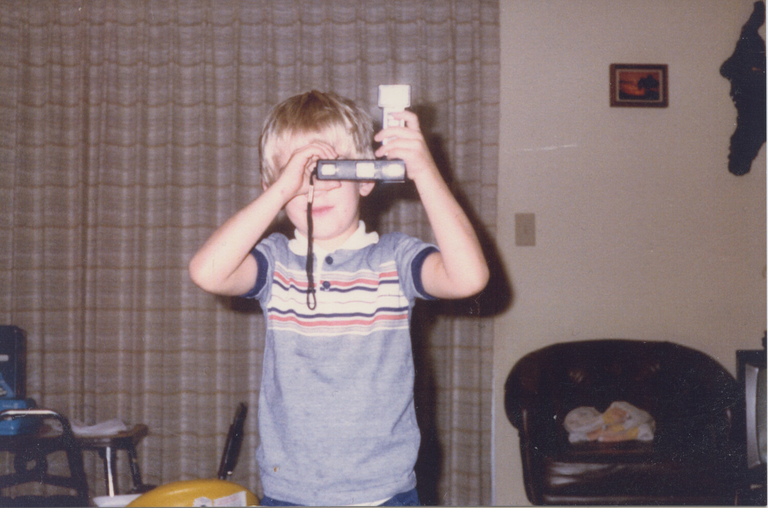 Jason Guffy at five years old, holding a 1980s film camera with a flash bar. The origin of the photographer. Jason Guffy Photography.