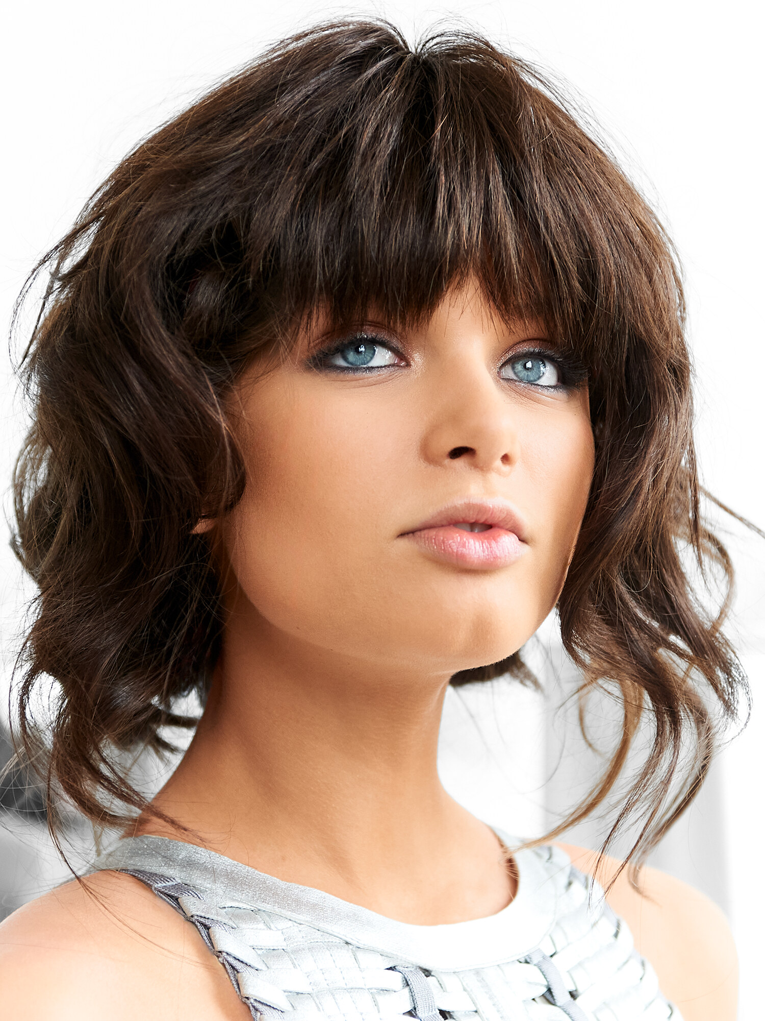 Close-up beauty portrait with blue eyes, textured bangs, and a metallic silver top in soft natural light. Beauty photography by Jason Guffy.
