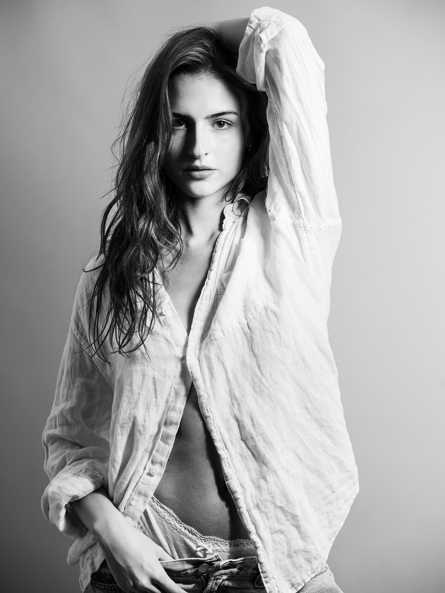 Black and white studio fashion portrait, tousled hair and an open white linen shirt with denim, soft studio light. Fashion photography by Jason Guffy.
