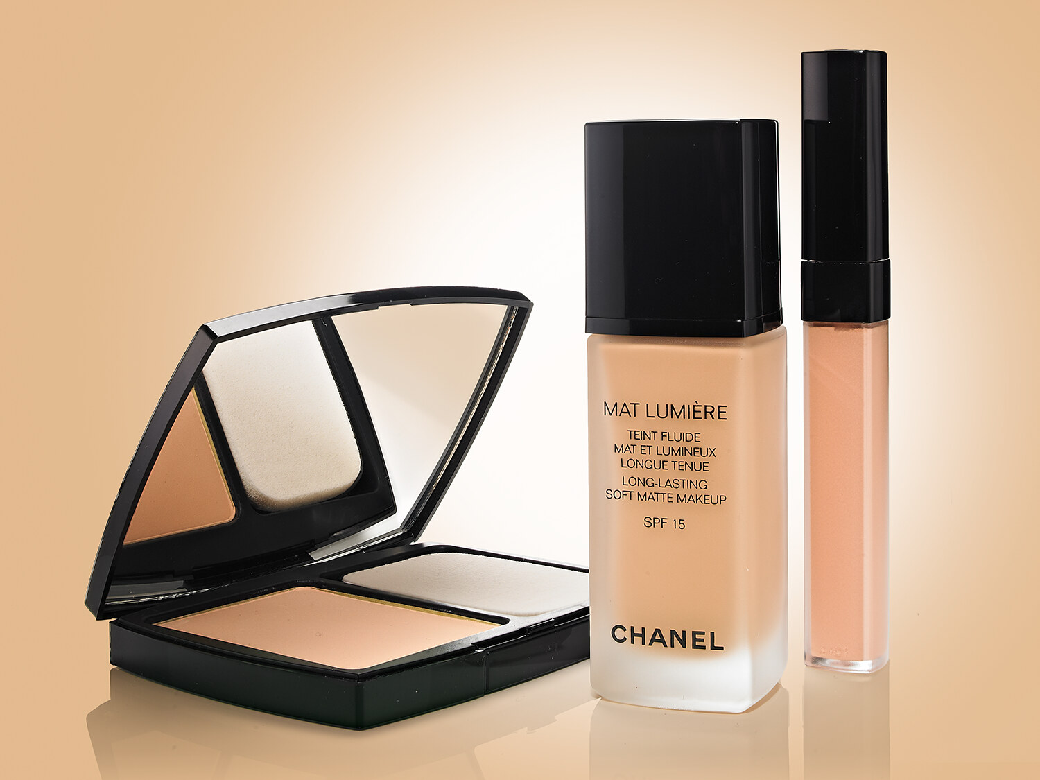 Chanel Mat Lumière complexion still life, fluide foundation with a powder compact and lip gloss on a warm gradient. Beauty product photography by Jason Guffy.
