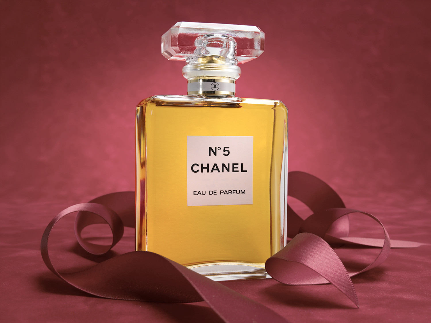 Chanel No 5 Eau de Parfum with coiled satin ribbon on a deep red backdrop. Fragrance product photography by Jason Guffy.