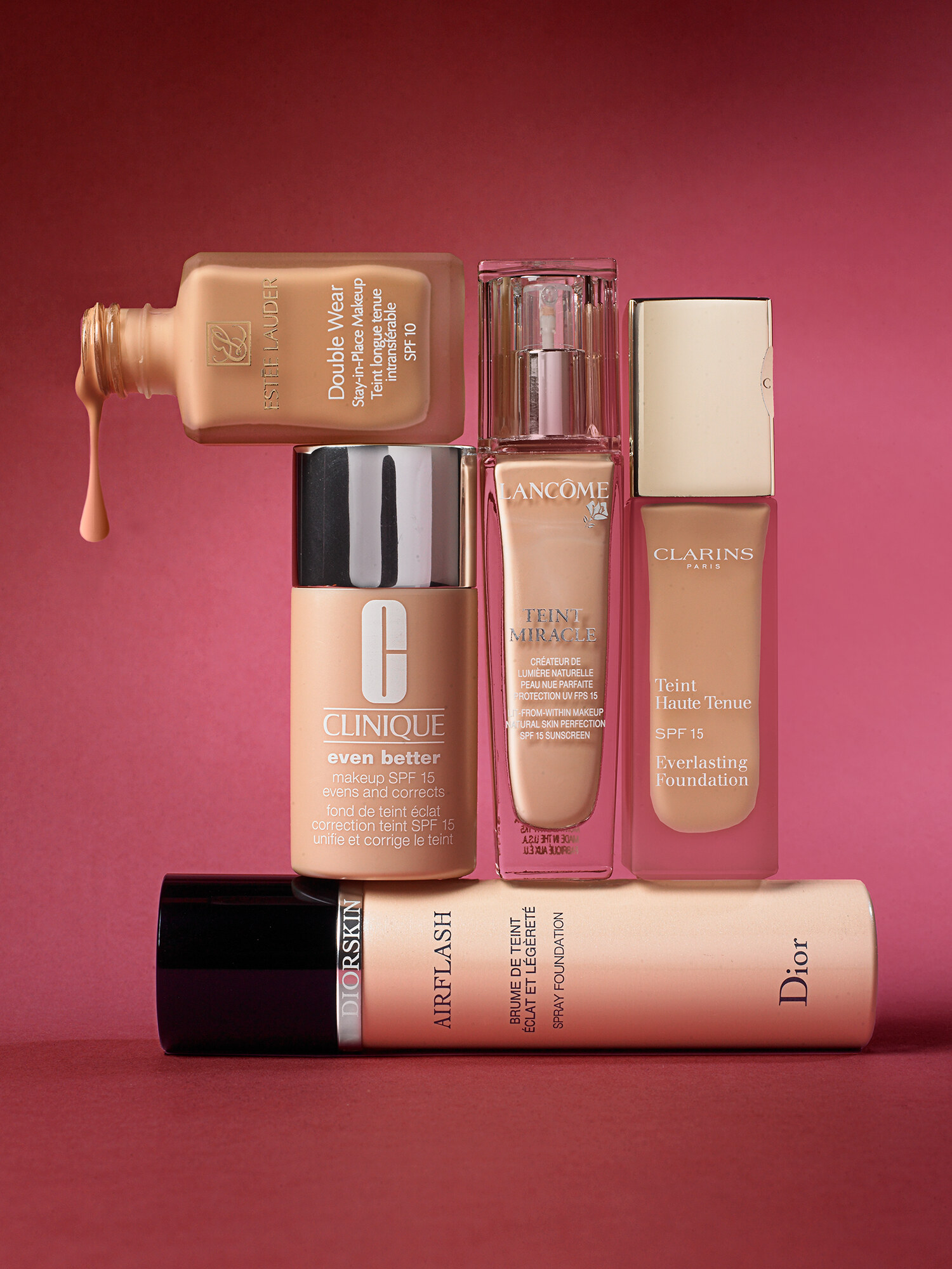 Beauty editorial product still life of luxury liquid foundations from Estée Lauder, Clinique, Lancôme, Clarins, and Dior on a deep red background. Beauty advertising product photography by Jason Guffy.