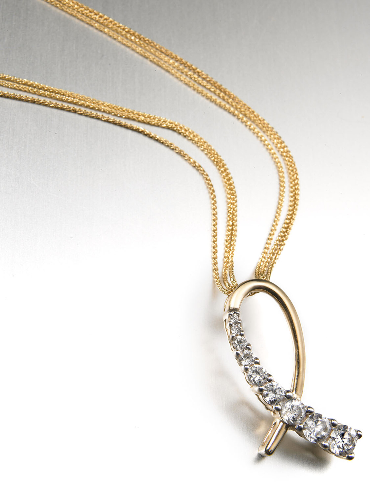 Fine jewelry still life of a diamond looped pendant on delicate gold chains over a soft silver gradient. Product photography by Jason Guffy.