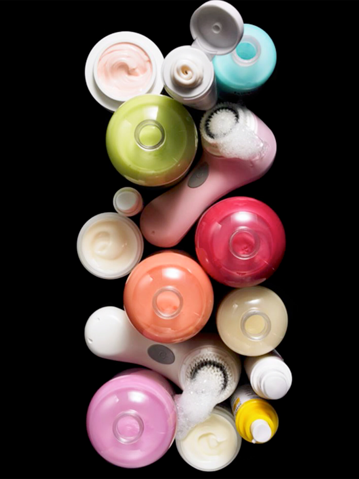 Overhead beauty still life of pastel skincare bottles, jars, and Clarisonic cleansing brushes arranged vertically on black. Macy's beauty campaign styled by Marissa Gimeno. Product photography by Jason Guffy.