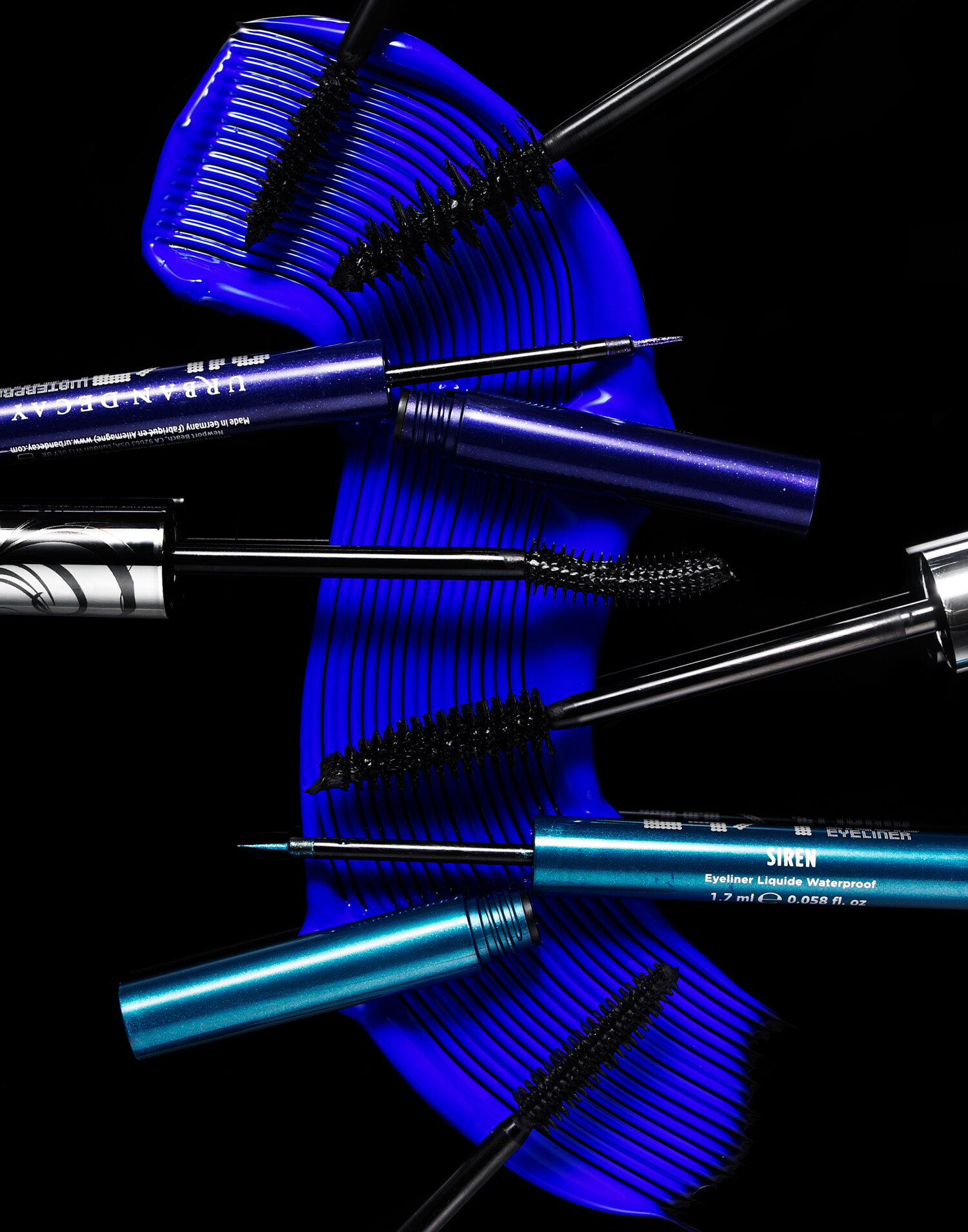 Editorial cosmetics still life of Urban Decay mascara wands and SIREN waterproof eyeliner on a bold blue brushed background. Beauty product photography by Jason Guffy.
