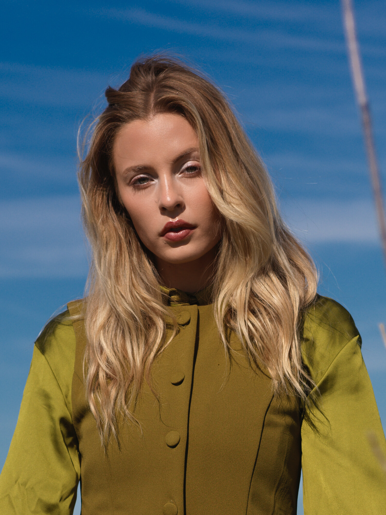 Fashion lifestyle editorial, a windblown close portrait in a grass field under blue sky. Fashion photography by Jason Guffy.