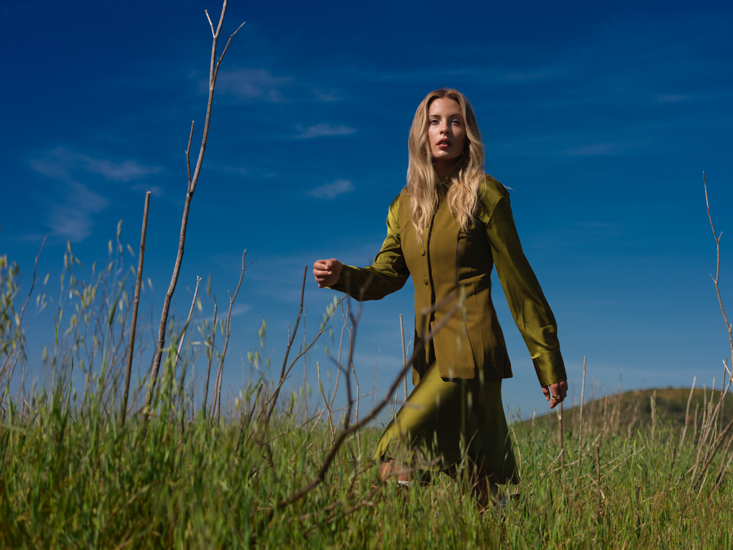 Fashion lifestyle editorial reaching through tall grass in an olive knit dress, open green field. Fashion photography by Jason Guffy.