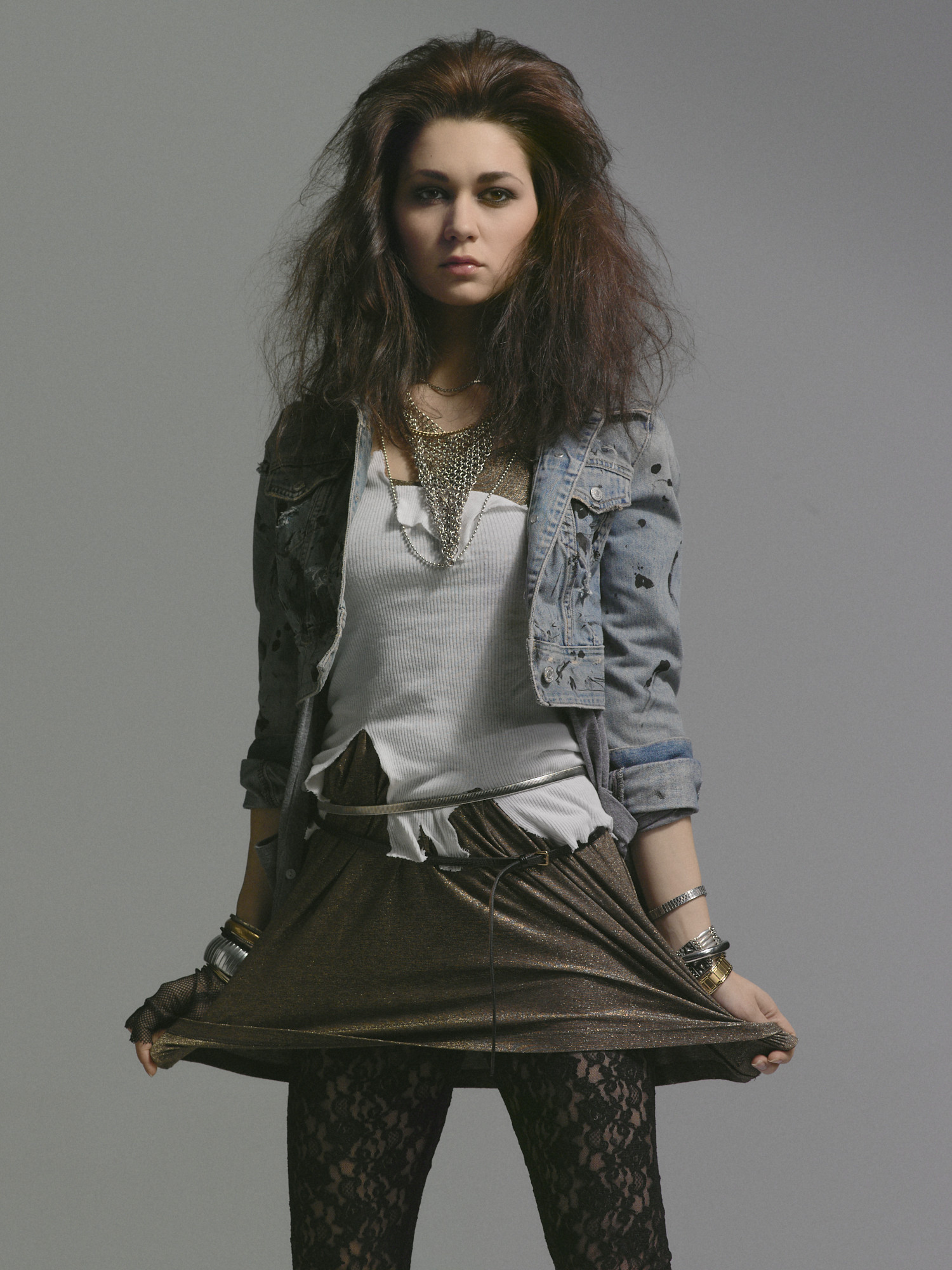 Studio rock editorial, three-quarter in a distressed denim jacket holding a bronze lame skirt with layered chains. Hair by DJ Quintero. Jason Guffy Photography.