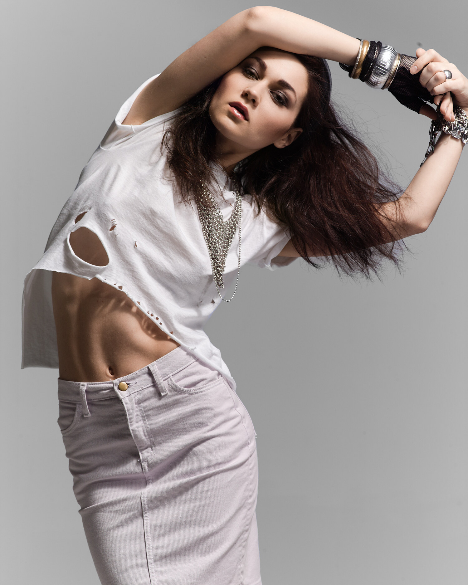 Studio fashion editorial in a distressed white tee, denim mini skirt and layered silver chains, hair by DJ Quintero. Fashion photography by Jason Guffy.